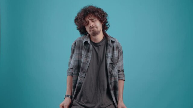 Sad employee without money, with curly hair. He takes out his pockets with his hands to show that he has no money.