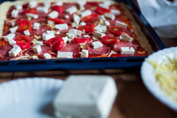 baking homemade pizza, woman adds cheese to pizza with olives and cherry tomatoes