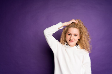 Naklejka premium Cheerful cute girl with wavy blond hair smiling and looking at the camera while standing on purple background