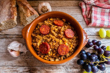 Fototapeta na wymiar Migas Manchegas with chorizo in a clay pot, served with grapes, garlic and bread. It is a Spanish dish, traditional from Castilla la Mancha.