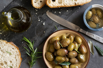 Italian sliced ciabatta bread on chopping board with herbs, extra virgin oil and marinated olives on dark grunge backdrop