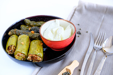 Stuffed zucchini with minced meat and rice. Stuffed leaves (yaprak sarma) presentation with yogurt, knife, fork and spoon on white background. Popular traditional food of Turkey and Middle East.