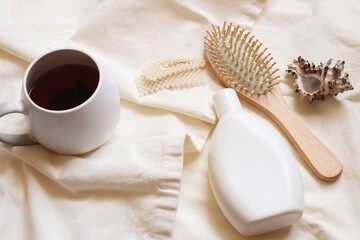 Obraz na płótnie Canvas White shampoo bottle, wooden comb and hairpin, cup of coffee. Morning beauty routine flat lay top view photography