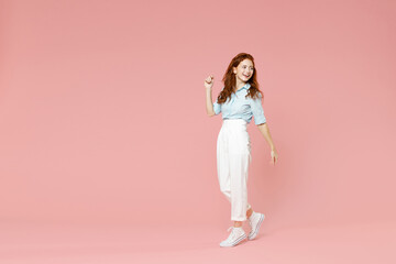 Fototapeta na wymiar Full length body of young student positive smiling happy caucasian redhead woman 20s wearing blue shirt pants walking going looking back aside isolated on pastel pink color background studio portrait.