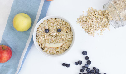 Cooked oatmeal with blueberries and apples. Funny face made of fruit. Art food.