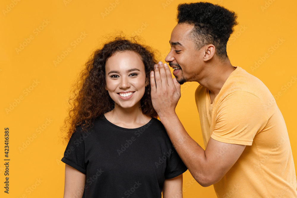 Wall mural young couple two friends family african surprised man woman in black t-shirt whisper gossip and tell