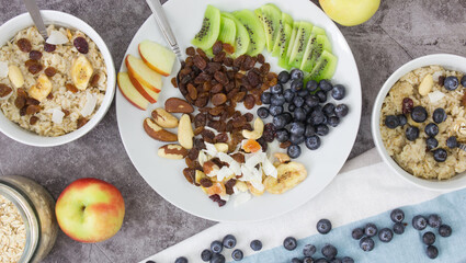 Cooking breakfast. Cooked oatmeal and a plate with dried fruits, nuts, fruits and berries on a gray background.
