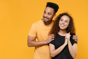 Young couple friends together family african pensive wistful woman man 20s in black yellow t-shirt boyfriend hug girlfiend look aside dream about future isolated on orange background studio portrait