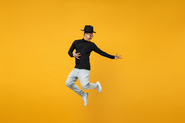 Fototapeta na wymiar Full length of young active singer overjoyed fun happy excited fun african man 20s in stylish black hat shirt eyeglasses jump high playing guitar isolated on yellow color background studio portrait.