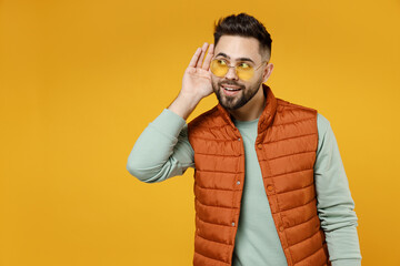 Young curious nosy caucasian man 20s wearing orange vest mint sweatshirt glasses try to hear you...