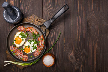 fried eggs with bacon and herbs on a frying pan top view