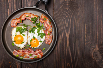 fried eggs with bacon and herbs on a frying pan top view