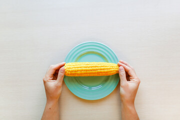 Sweet corn in female hands on the plate. Summertime