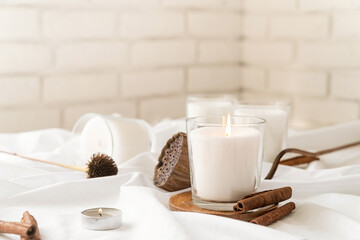 Beautiful burning candles with cinnamon and dry flowers on white fabric background