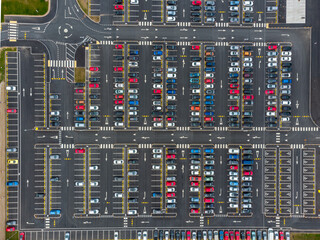 Busy large modern carpark with symmetrical roads rows of parking bays lots of symmetry and colours aerial view from drone up above looking down on tarmac asphalt car storage 