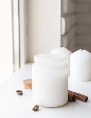 Beautiful white candle with cinnamon sticks and coffee beans on white background. Mock up design
