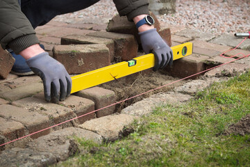 Close view of a working man holding a level tool and restoring the paving stones of the terrace. Gardening work.
