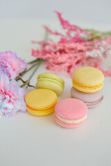 Macarons and flowers on a white background. Colorful french dessert with fresh flowers. Top view
