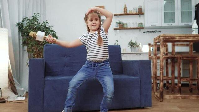 little child daughter a sing dancing at home. stay home active leisure happy childhood concept. child daughter dancing sing next to the sofa with a microphone dream. kid dream dance