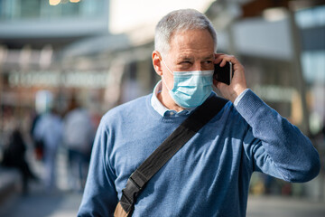 Covid coronavirus concept, masked man talking on his smartphone outdoor