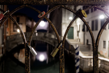 Photograph of a railing of a bridge in Venice taken at night with padlocks attached