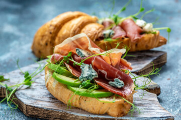 Croissant sandwich with jamon ham serrano paleta iberica, blue cheese, avocado, microgin on blue background. Food recipe background. space for text. top view