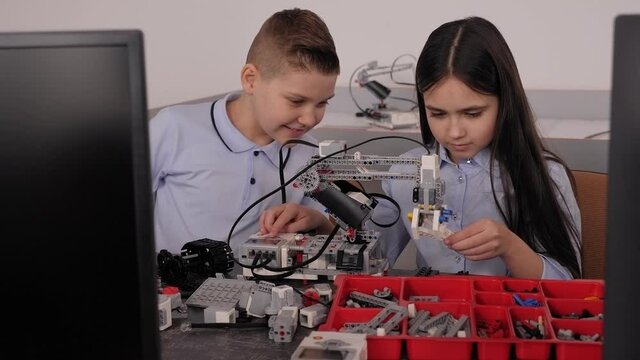 Children makes a robot from the robotic constructor at the desk with computer.