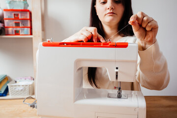 Closeup woman's hands tucks the thread into the sewing machine