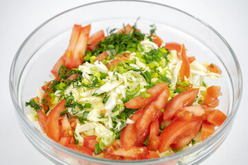 fresh salad with cabbage, tomatoes and greens in a glass bowl