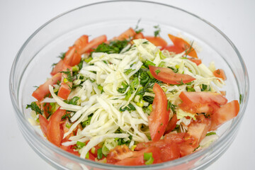 fresh salad with cabbage, tomatoes and greens in a glass bowl