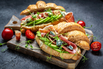 Croissant with prosciutto, amon, blue, cheese, avocado, microgin and cherry tomatoes. Mediterranean appetizer. Breakfast concept