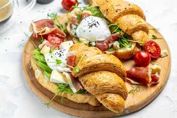 Croissant with prosciutto, poached egg, jamon, blue, cheese, avocado, microgin and cherry tomatoes on a light background, Cup of coffee, top view