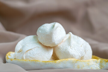 Homemade meringue in the form of a drop on a hand-made white-gold plate on a delicate brown background. Basic crispy preparations for the Anna Pavlova cake