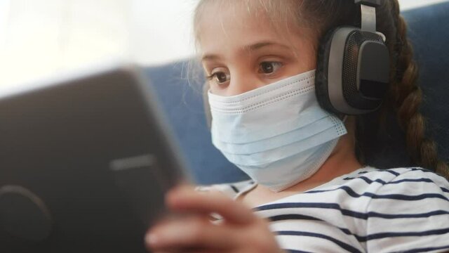 distance learning online lessons. child girl with digital tablet in mask studying remotely at home. education coronavirus online lessons lockdown concept. child learns distance learning school