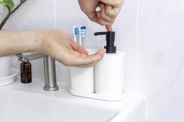 Man's hand pressing white bottle hand sanitizer in the bathroom isolated on white background