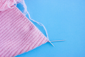 knitting needles and pink pattern of yarn on a blue background, home hobby.