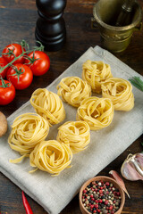 Raw pasta tagliatelle with fresh tomatoes, peppers, asparagus beans, spices and cheese on wood background.