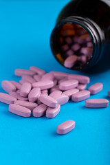 Pink pills are scattered from a glass jar on a blue background.  Health care concept. Space for text. Conservative medicine.