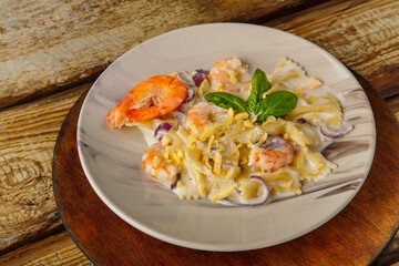 Pasta with shrimps in a creamy sauce, garnished with spinach on a gray plate on a wooden table on a round stand.