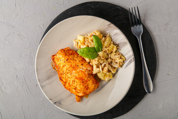 Baked chicken breast with salad on a plate decorated with spinach next to a fork on a gray background on a round black stand.
