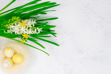 Spring, Easter concept. Yellow Easter eggs in a nest next to a bouquet of daffodils on a white concrete table. Place for an inscription. The basis for the coating.