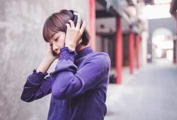 Fototapeta premium Happy young asian woman listening to music with headphones on the street.