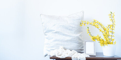 Spring, easter mockup. Empty wooden picture frame. Branches of yellow forstythia flowers in white vase. Soft pillow, knitted foular. Soft colors in the natural sunlight of italian design interior