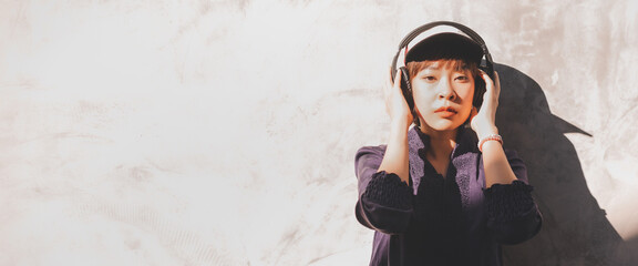 Happy young asian woman listening to music with headphones on the street. Banner background