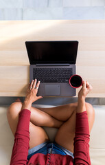 Young girl working at home with a laptop while holding a cup of coffee