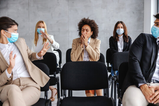 Ill businesswoman coughing while sitting with her colleagues on seminar. Colleagues afraid of corona virus so they hiding.
