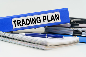 On the table are a notebook, a pen, documents and a folder with the inscription - TRADING PLAN
