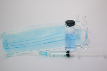 Vial vaccine, glass ampoules and a syringe with medical protective mask on white background, global vaccination concept