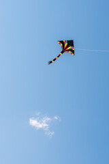 Naklejka na ściany i meble Colorful kite flying against blue sky with a single cloud