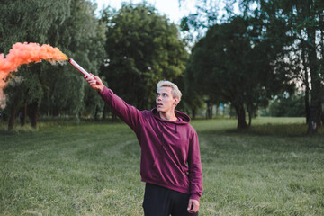 Street style man in hoodie hold hand flare with red smoke grenade bomb.